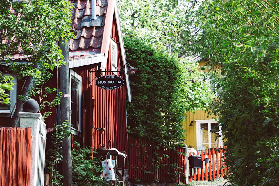 Rotes und gelbes Holzhaus zwischen grünen Bäumen in Vaxholm, Schweden – Foto: Daniel Welsh